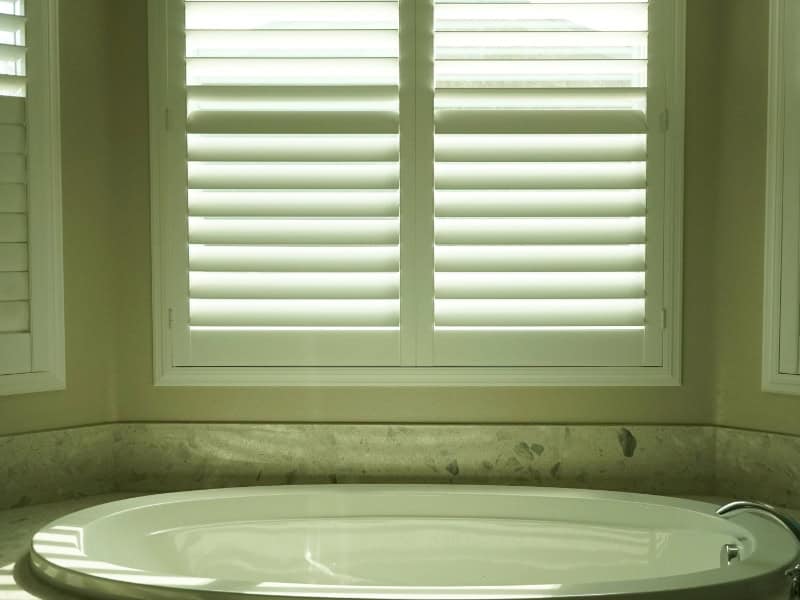 plantation shutters in bathroom above bathtub with natural light