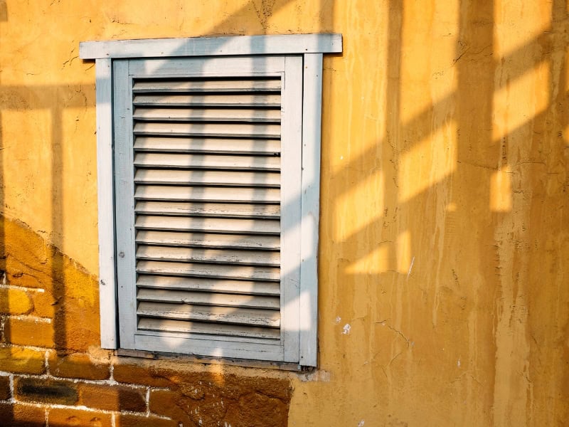 Rustic outdoor window with faded blue frame showing effects of installing plantation shutters.