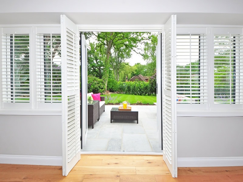 Types of indoor shutters in white plantation design framing patio doors and side windows.