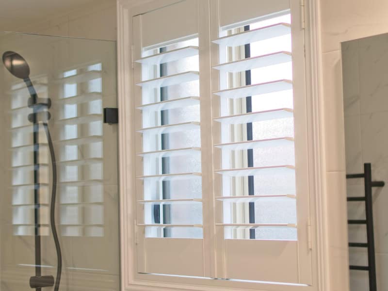 plantation shutters in bathroom window beside shower enclosure