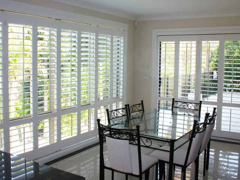 Bright dining room after installing plantation shutters on large glass windows.