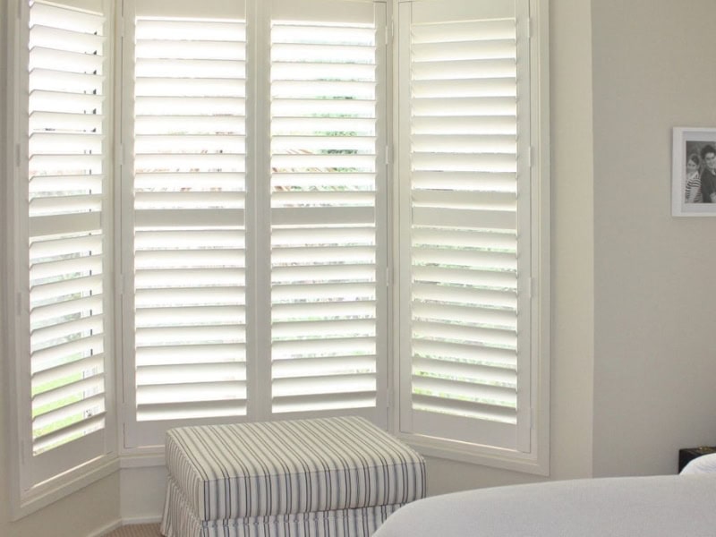 Bedroom bay window featuring privacy and light control from installing plantation shutters.