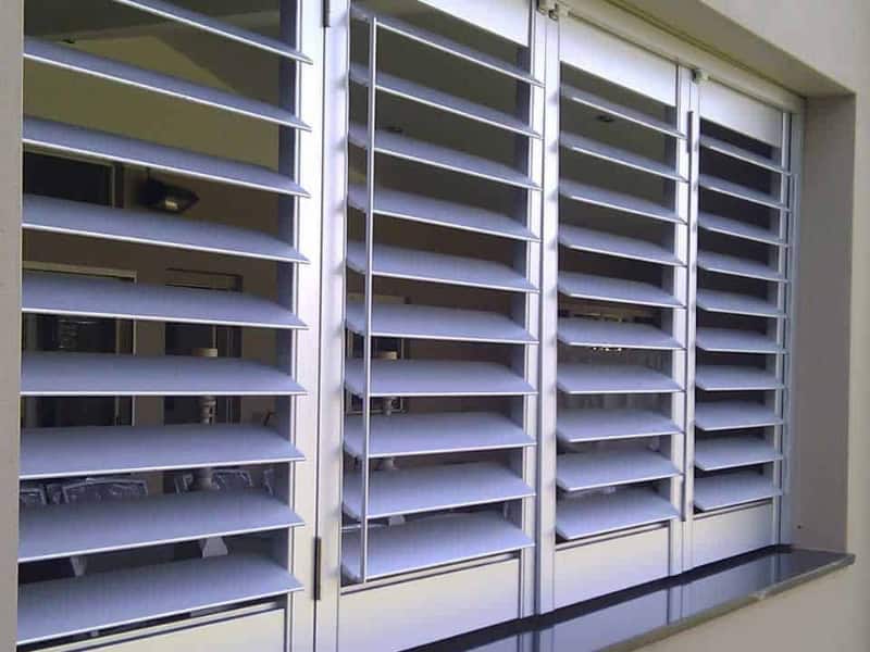 Small window shutters in silver aluminium featuring wide adjustable louvres for improved airflow, privacy, and exterior light regulation.
