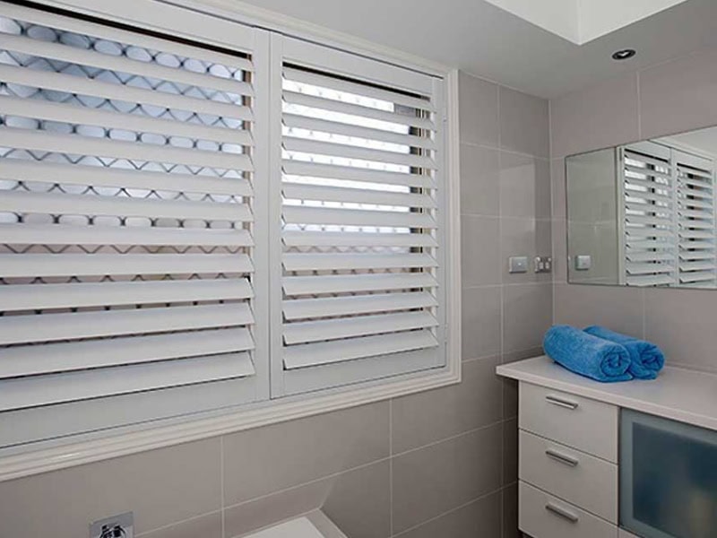 White plantation shutters for interior windows installed in a modern bathroom, providing privacy, ventilation, and soft natural light.