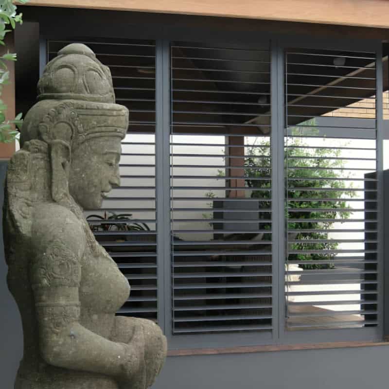 External Aluminium Plantation Shutters installed on outdoor windows beside a decorative stone statue in a modern home.