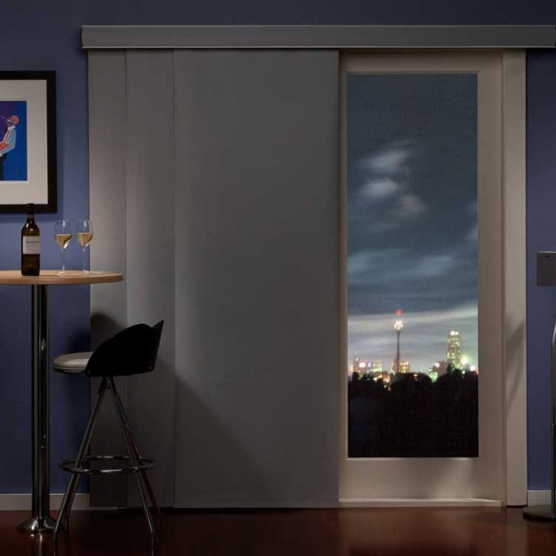 Panel blinds covering large sliding door in modern room, partially open revealing night city skyline view.