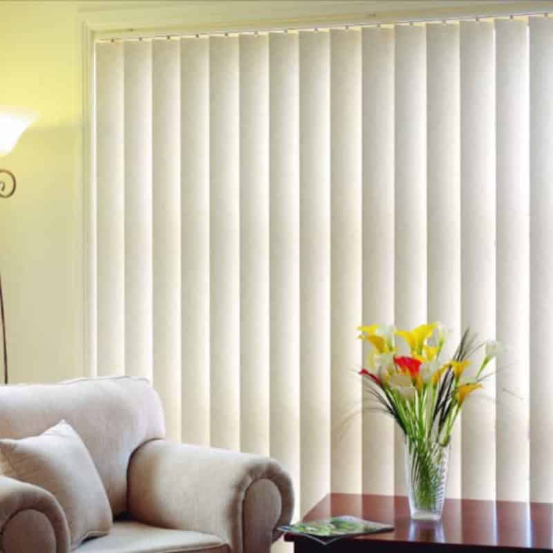 Cream vertical blinds covering sliding door behind sofa and side table with flowers in bright living room