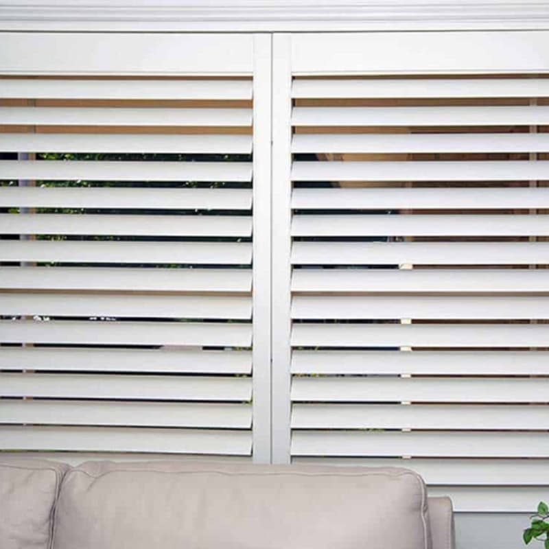 White indoor plantation shutters with horizontal louvres behind sofa in modern living room interior