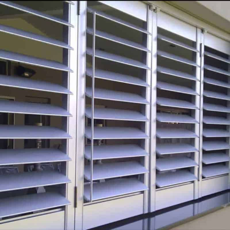 White outdoor plantation shutters with adjustable louvres installed across exterior windows of modern home