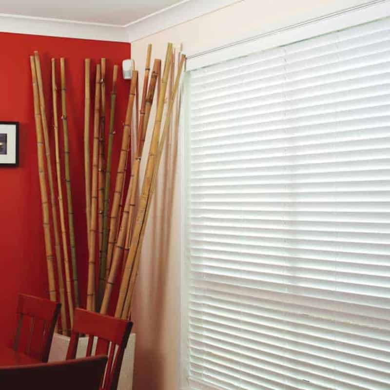 Venetian blinds covering a bright window beside bamboo décor and dining furniture in a warm interior space.