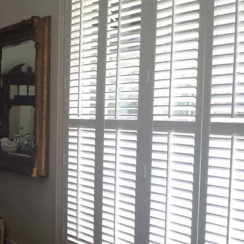 Interior plantation shutters on tall windows with white louvres, offering bright light control and privacy.